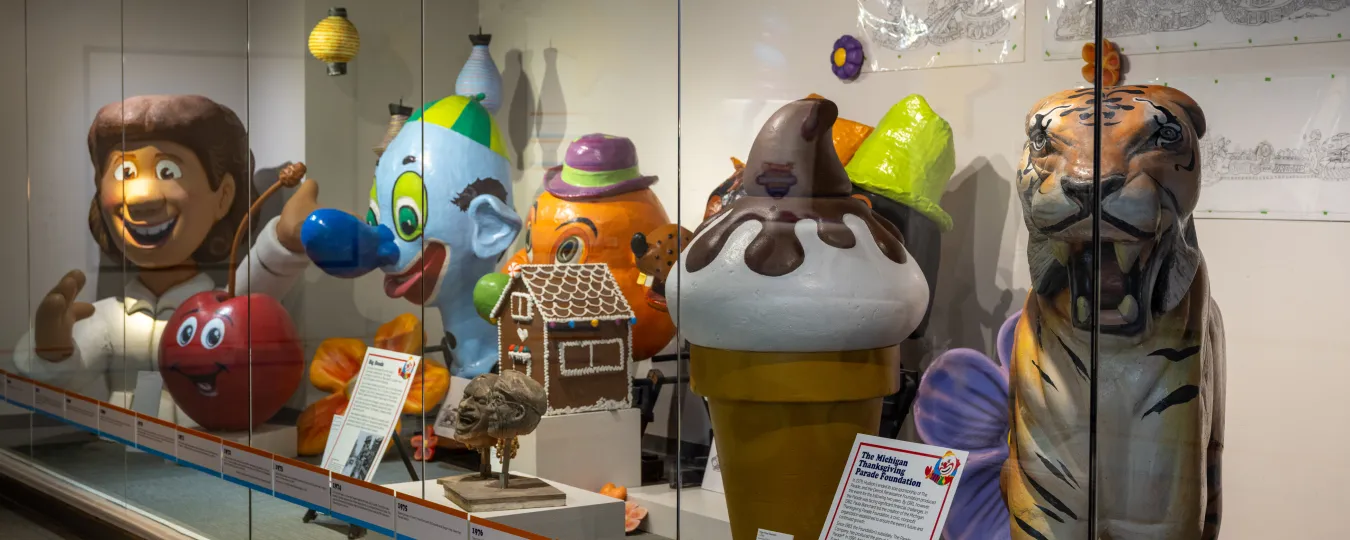 Colorful parade balloons and decorations displayed in a glass case exhibit.