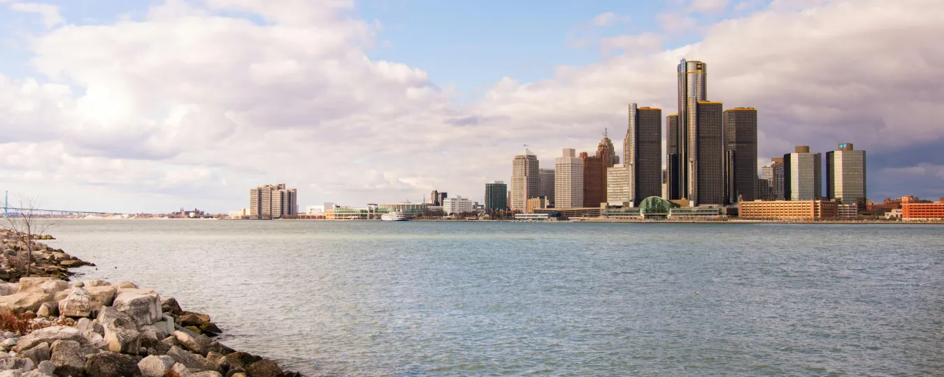Riverfront skyline with city buildings under a blue sky with clouds.