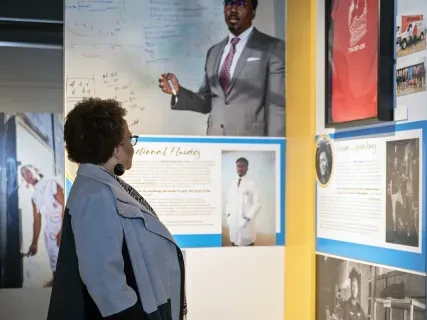 Woman observing a museum exhibit with portraits and informational panels.
