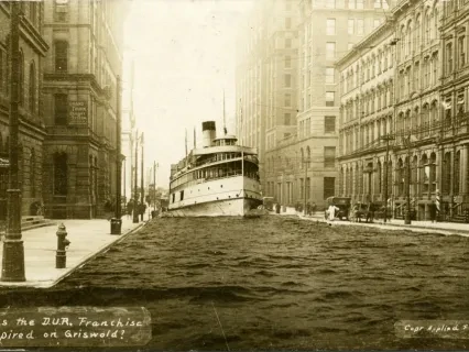 A large ship appears to be navigating down a flooded city street between tall buildings, sepia-toned photograph.