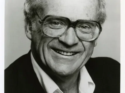 Smiling man with glasses in black and white portrait.