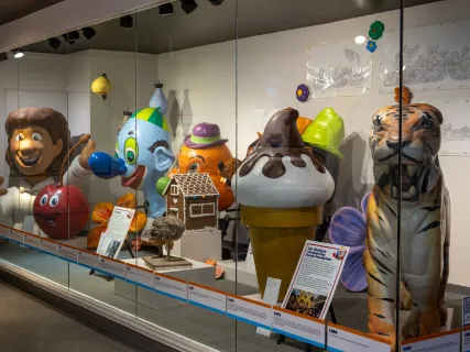 Colorful parade balloons and decorations displayed in a glass case exhibit.