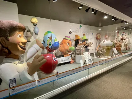 Parade balloon replicas displayed in a glass case at a museum exhibit.