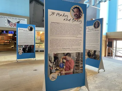 Exhibit panels with text and photos stand in a spacious room with light walls and windows.