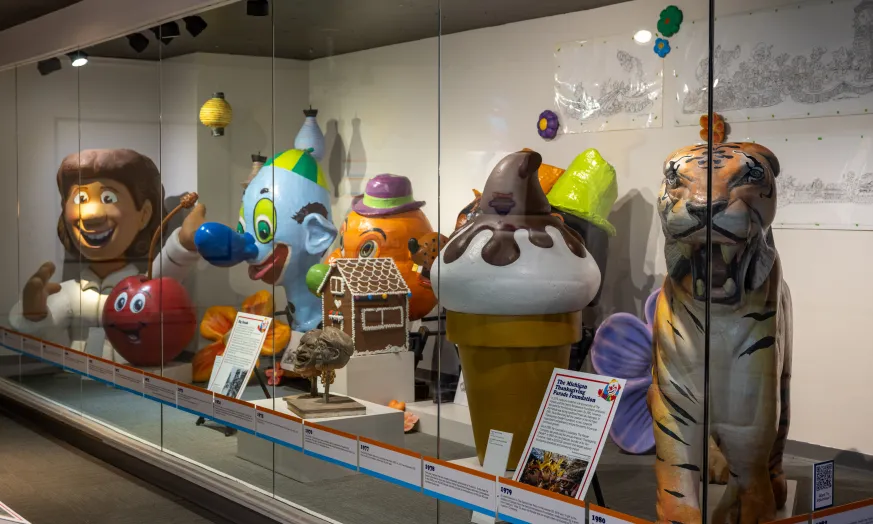 Colorful parade balloons and decorations displayed in a glass case exhibit.