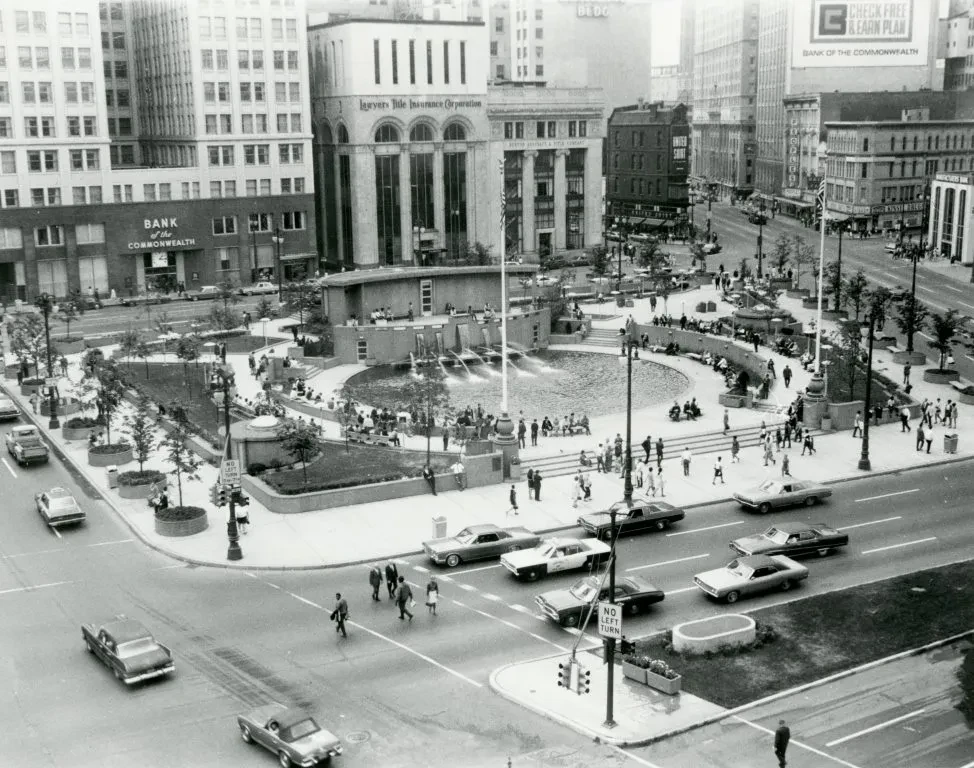Historic city square with cars and pedestrians, surrounded by tall buildings.