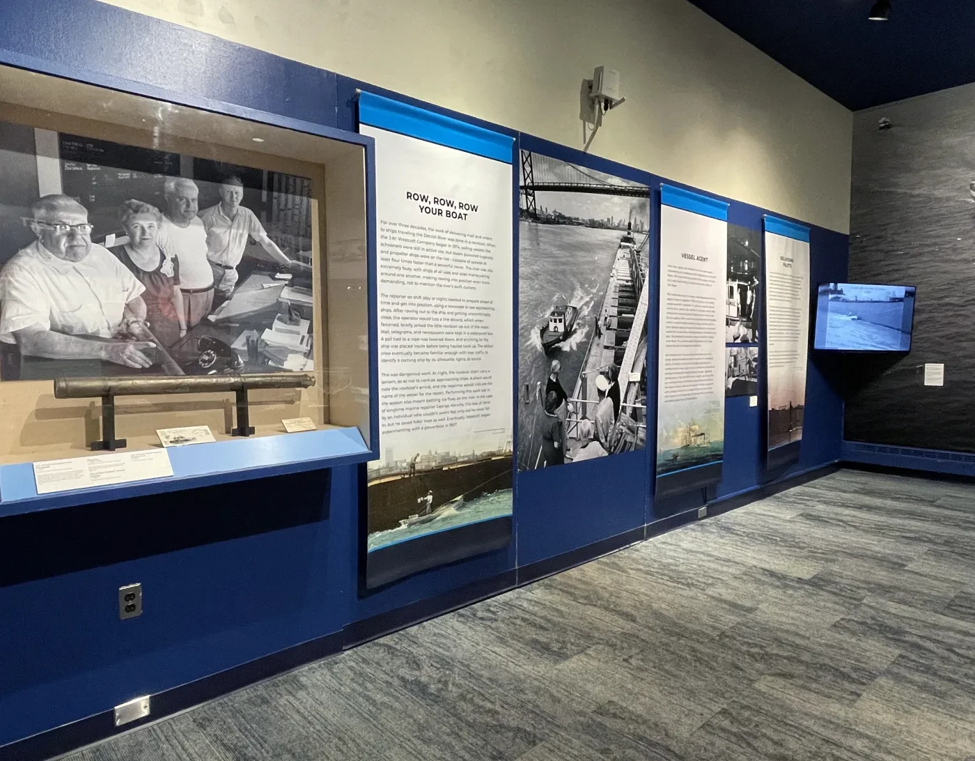 Museum exhibit wall with photographs and text panels under dim lighting.