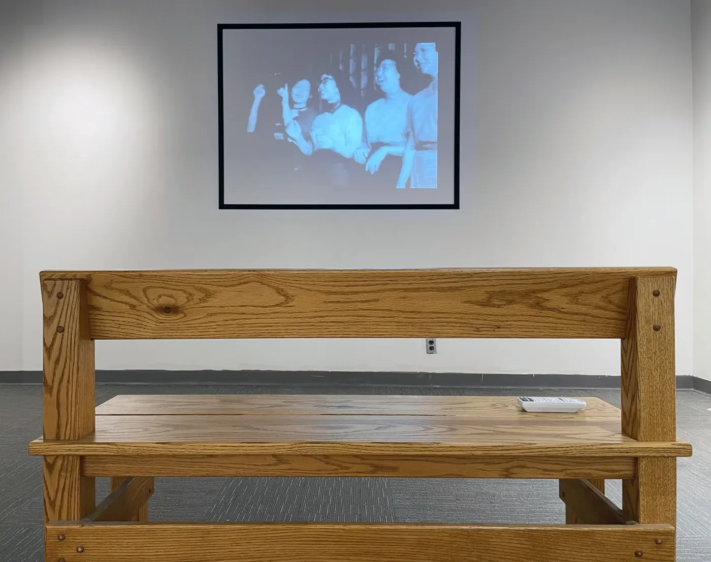 Wooden bench facing a black-and-white photograph on a wall in a gallery setting.