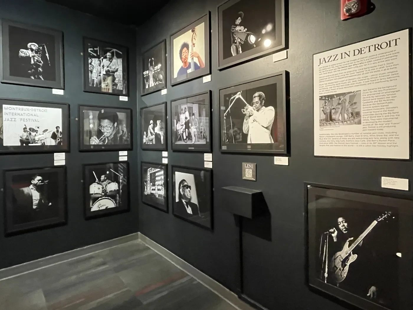 Black and white photographs of musicians on a dark wall in a gallery setting.