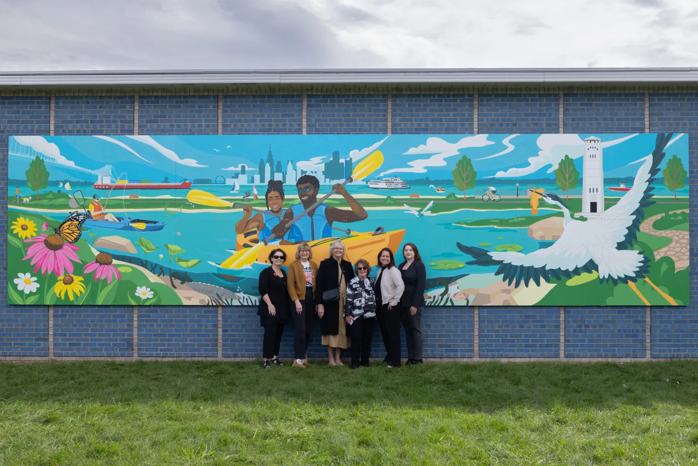 Mural depicting people kayaking and nature; group of people standing in front on grass.