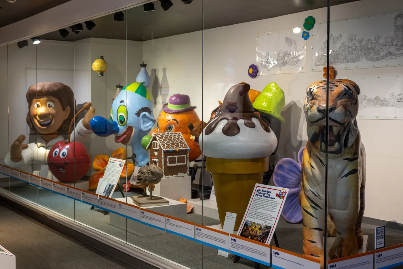 Colorful parade balloons and decorations displayed in a glass case exhibit.