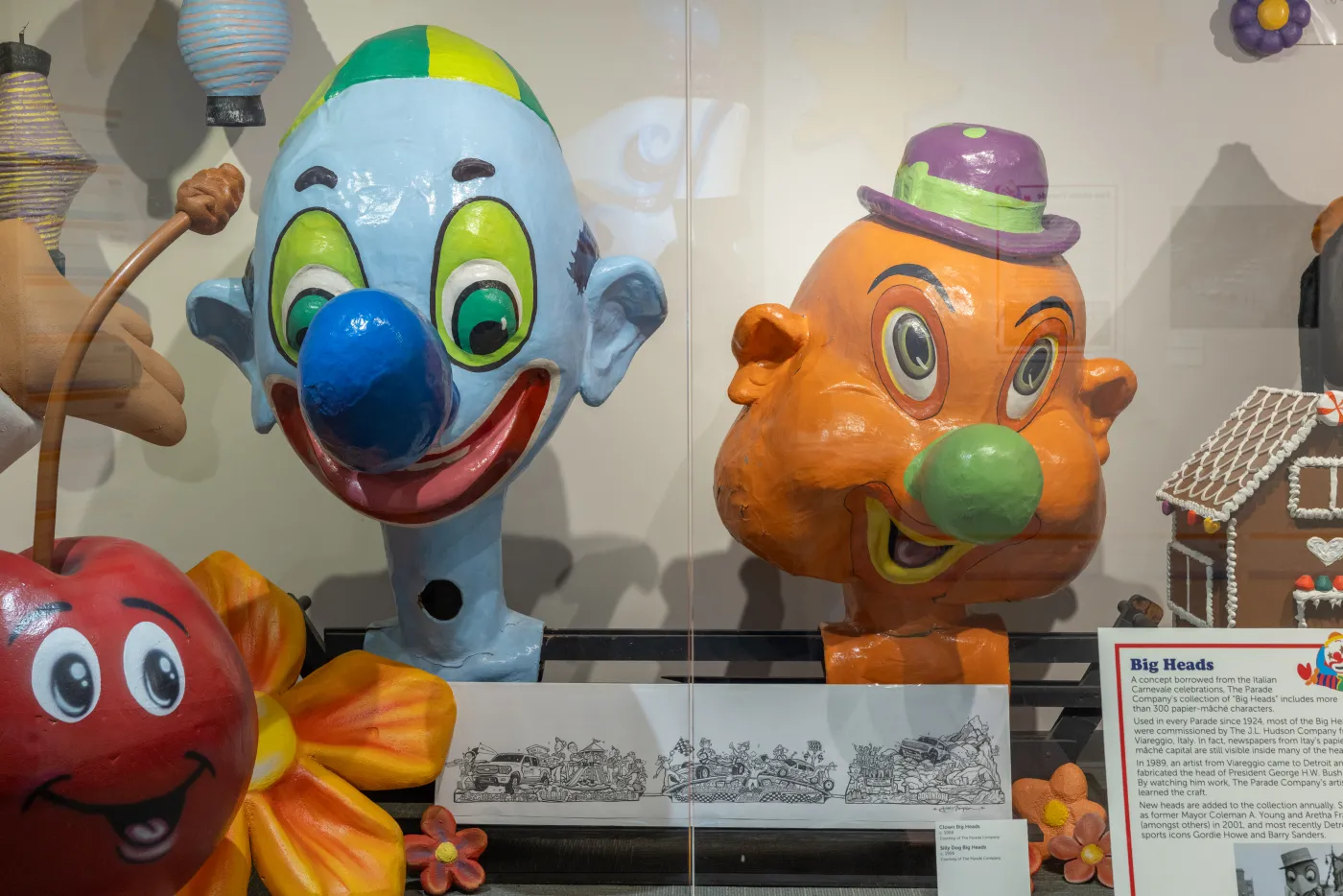 Two colorful clown heads on display, one blue with a cap and one orange with a hat, surrounded by other playful objects.