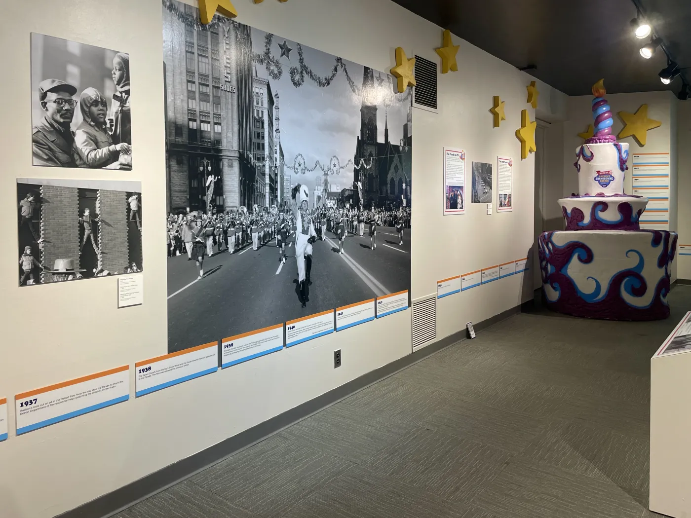 Museum exhibit with large black-and-white photos and a colorful, multi-tiered, decorative cake sculpture on the right.