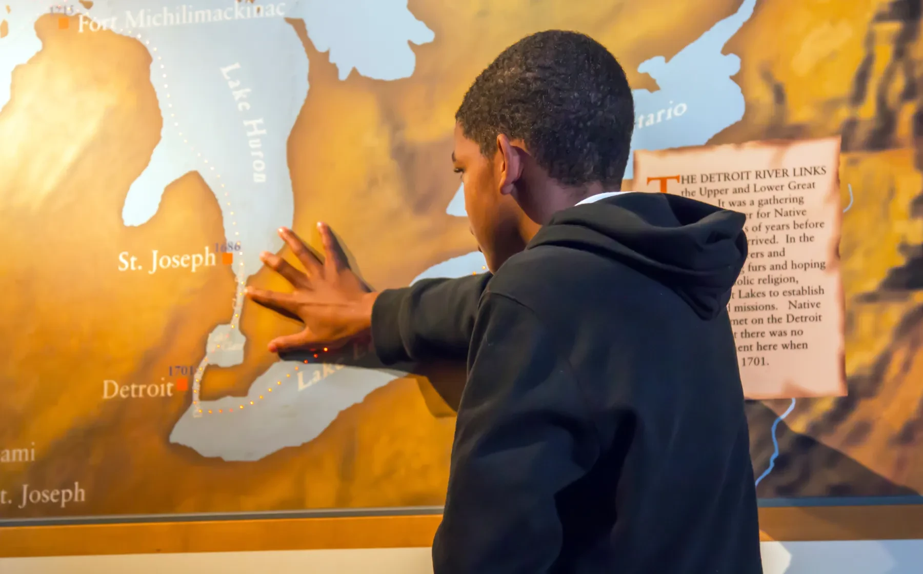 Boy touching a tactile map on a wall, engaging with map textures.