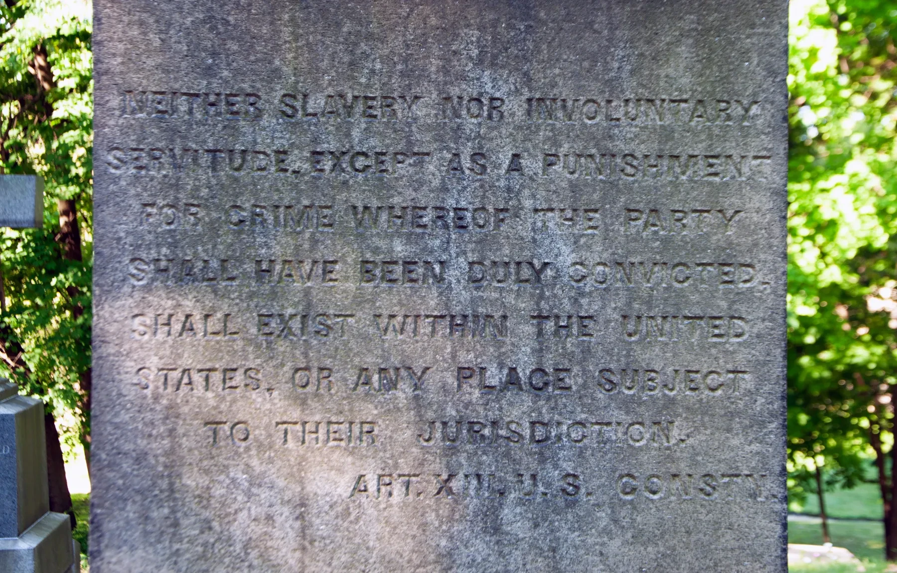 Stone monument with engraved text about slavery abolition, surrounded by greenery.