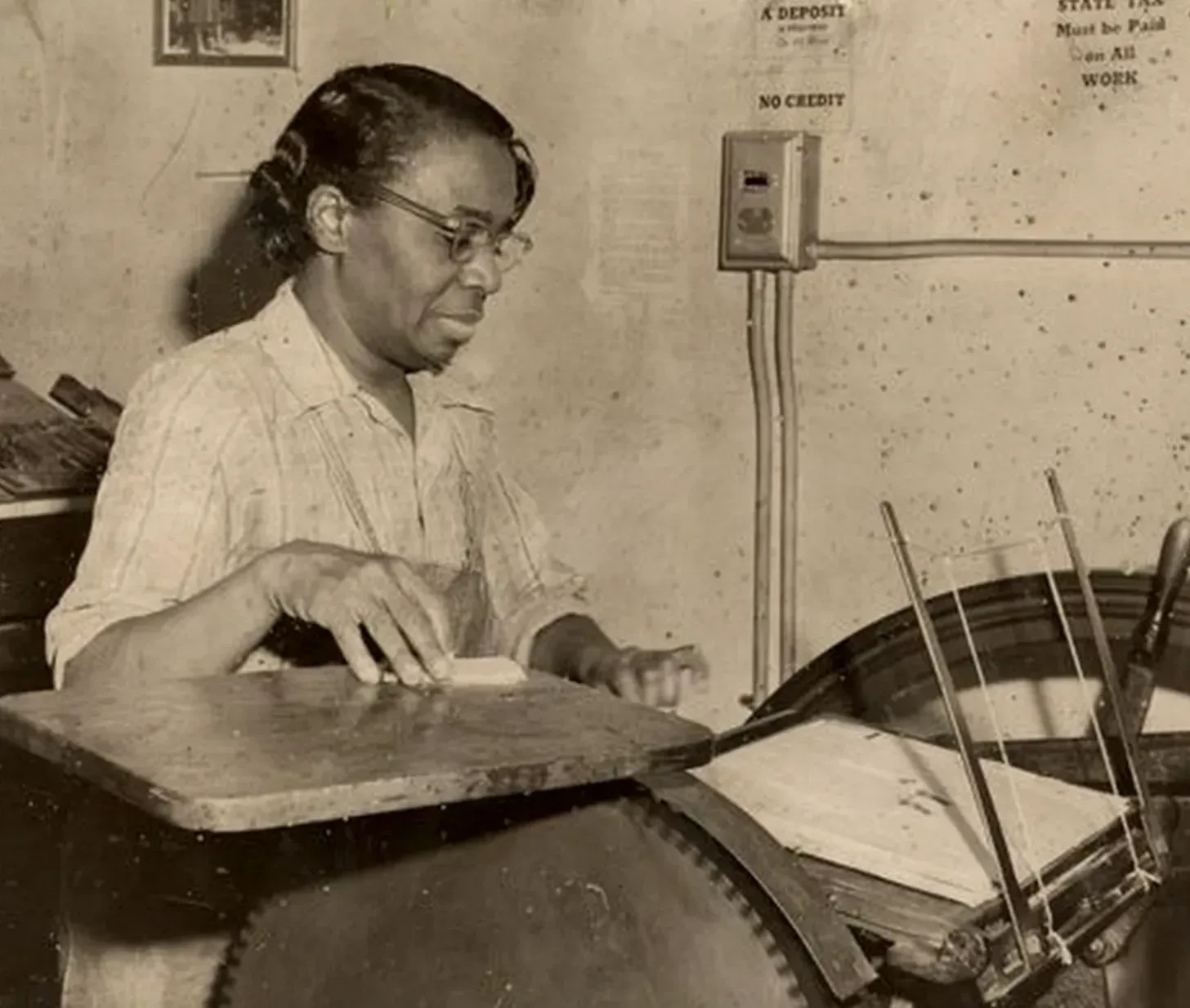 A woman operates a vintage printing press, focused and working.