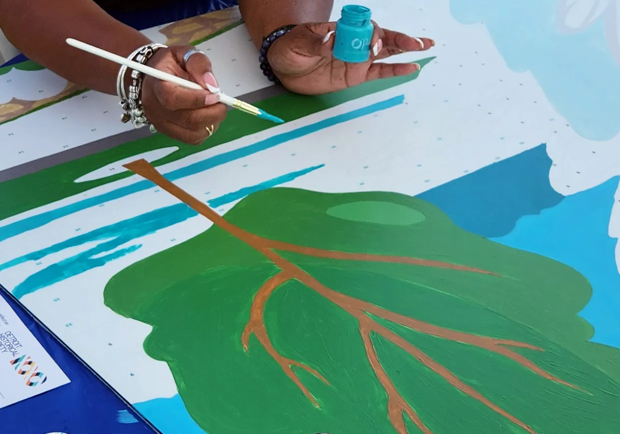 Hands painting a leaf on a vibrant mural, using green and blue acrylics.